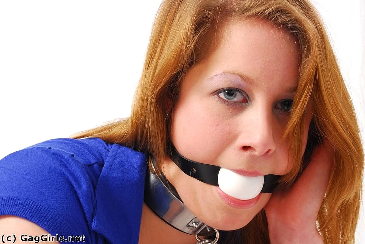 Natural redhead grasps her ankles while fully clothed and ball gagged